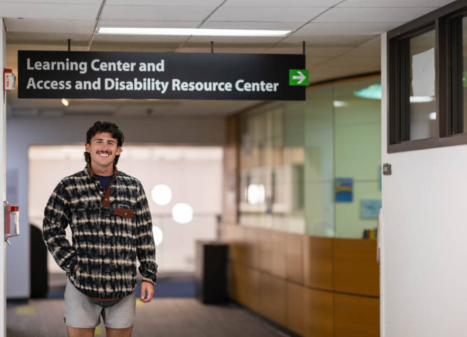 Tristan Lebourhis stands beneath the sign for the Access and Disability Resource Center.